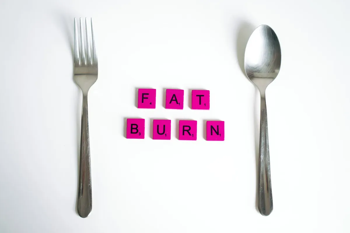 白い背景上にフォークとスプーンの間にあるスクラブルタイルが「Fat Burn」という文字を形成した概念芸術。