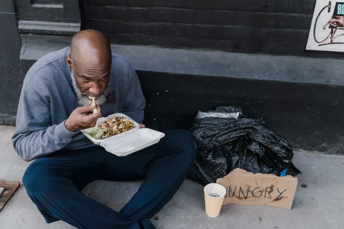 ホームレスな男と食品容器と「飢えた」サインが sidewalk に