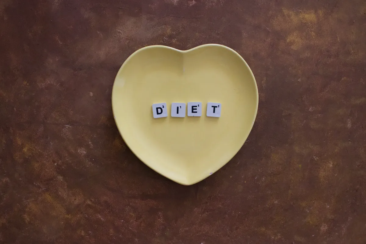 形狀如心的黃色盤子上擺著拼寫「Diet」的 Scrabble 砖塊，背景為棕色質感。