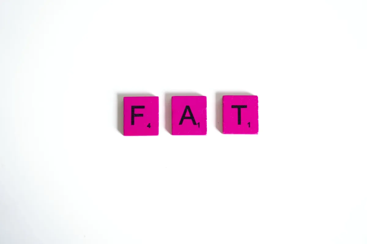 Pink Scrabble tiles spelling 'FAT' on a clean white background, showcasing typography art.