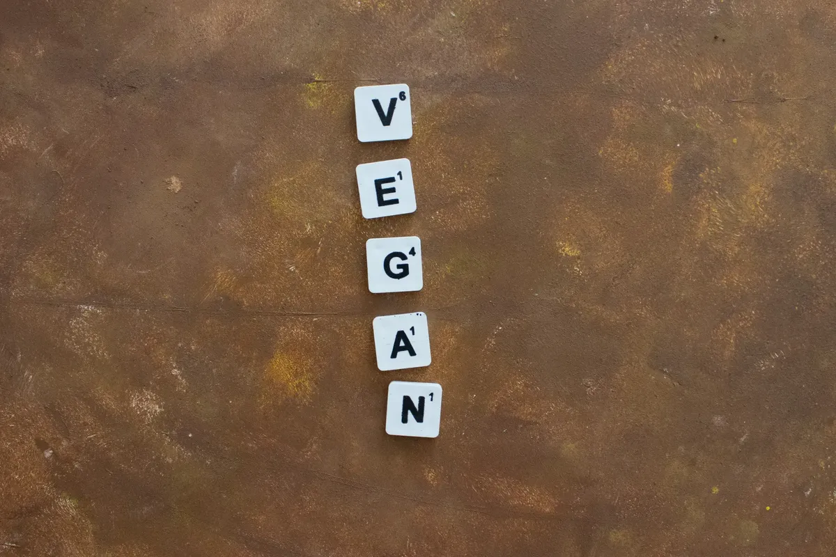 A creative arrangement of Scrabble tiles spelling 'Vegan' on a rustic brown background, emphasizing a plant-based lifestyle.