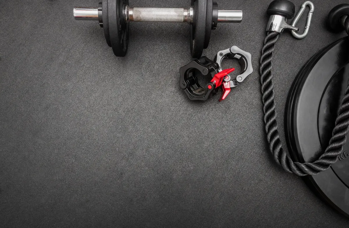 Flat lay of gym equipment including a dumbbell, weights, and rope on a dark surface ideal for fitness themes.