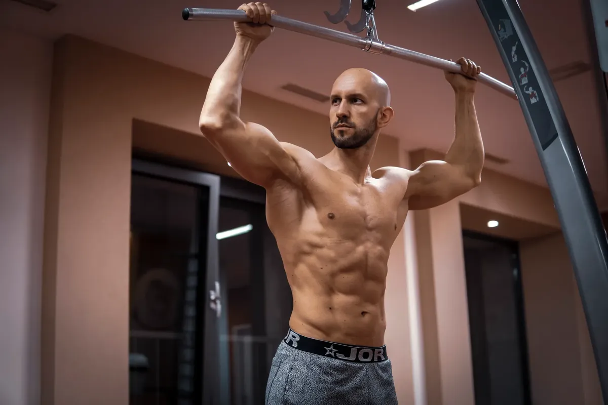 A bald, muscular man performing exercise on gym equipment indoors.